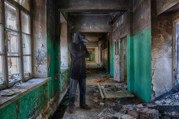 Tall man in leather plague doctor  mask and mantle with hood inside abandoned building. Monster or ghost for horror
