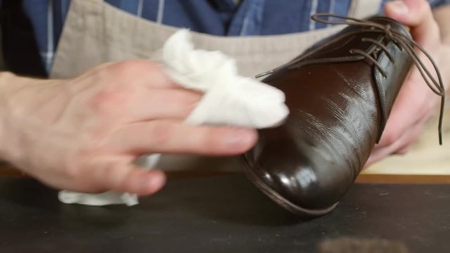 Close up shot of hands of male shoemaker polishing elegant leather boot with cloth wrapped around fingers