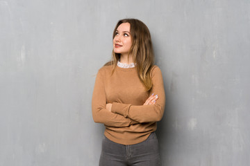 Teenager girl over textured wall looking up while smiling