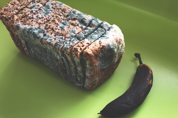Top view of moldy sliced bread and spoiled banana on green kitchen counter.