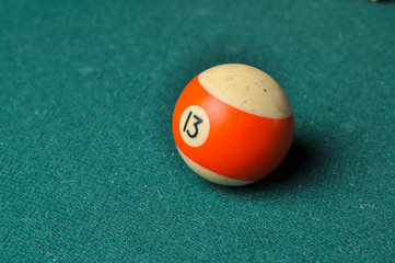 Old billiard ball number 13 striped white and orange on green billiard table, copy space