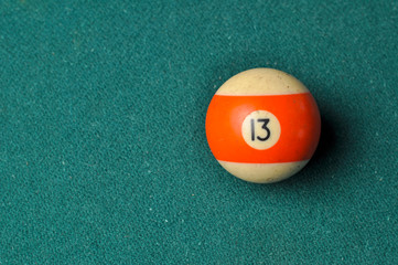 Old billiard ball number 13 striped white and orange on green billiard table, copy space