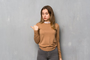 Teenager girl over textured wall unhappy and pointing to the side