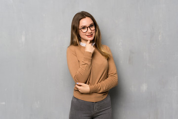 Teenager girl over textured wall with glasses and smiling