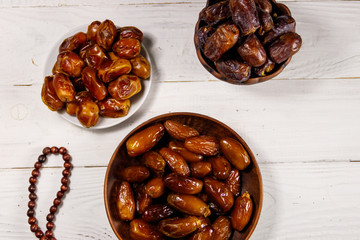 Dates fruit and rosary on white wooden table. Top view