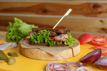 juicy sandwich with grilled dark bread and bacon wait for you on wooden plate