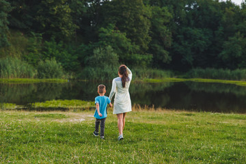 mother with kid holding hands walking to lake