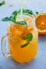 jar of fresh orange juice with orange slices, ice, mint leaves on a gray background