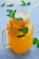 jar of fresh orange juice with orange slices, ice, mint leaves on a gray background