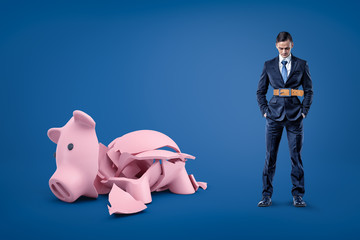 Businessman wearing tight belt and broken piggy bank on blue background
