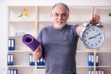 White bearded old man employee doing exercises in the office 