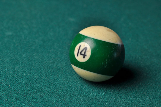 Old billiard ball number 14 striped white and green on green billiard table, copy space