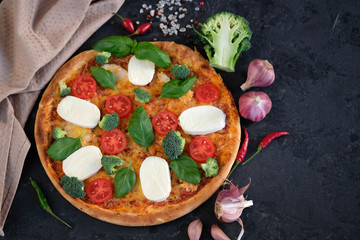 Italian pizza with Mozzarella cheese, tomatoes, broccoli, Spices and fresh basil. Pizza and kitchen napkin near, on black stone background