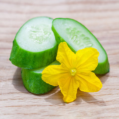 Close up view on a slices of fresh cucumber with yellow flower lying on a wooden table (shallow...