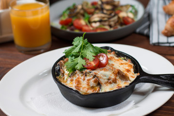 Grilled eggplant stuffed with tomatoes, nuts, pomegranate and herbs and cheese, baked in a black pan. Wood background