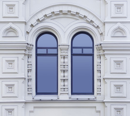 Close up view on a facade of white ancient building with decorative ornaments and two-part arched windows as texture