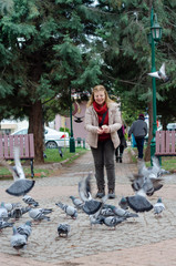 Blonde woman is feeding pigeons.