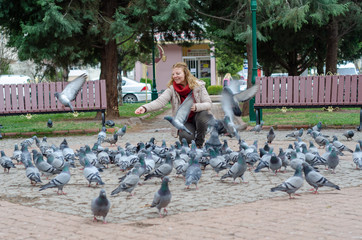 Blonde woman is feeding pigeons.