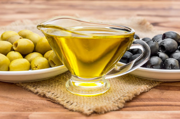 Gravy boat with olive oil and saucers with olives on the table.