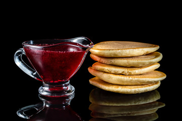 Pancakes and gravy boat with jam on black reflective background.