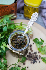 Green adjika. Traditional Georgian spice blend, mix of spices with fresh green coriander, hot chilly pepper in glass jar on wooden board. Food from Georgia.
