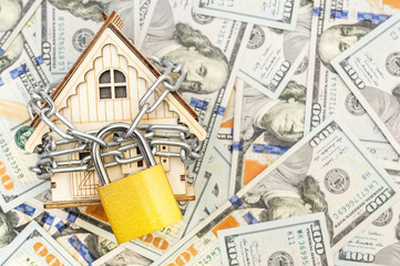Model of house locked by chain with padlock on background of dollar bill. Top view. Space for text.
