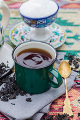 Black tea in green enamel mug or cup on napkin with teapot. Whole leaf hot tea drink. Potluck ot tea party.