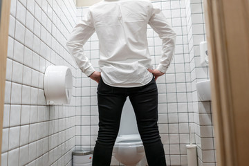 back view of businessman piss in front of the toilet in the bathroom