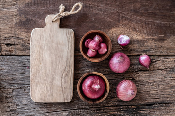 Top view of herbal vegetable ingredients, fresh red onion and empty chopping board on old wooden table, cooking preparation concept