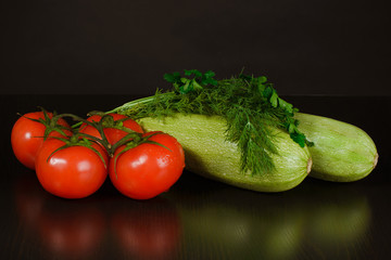 Red tomatoes, two ripe zucchini and fresh juicy parsley and dill on a black background, reflection on the table
