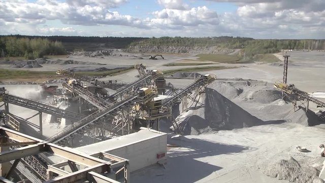 Mining industry.  Mining site conveyors of gravel in a quarry. Powerful red excavator with a full bucket of crushed stone on a background of constructions of mining enterprise. Heavy mining equipment