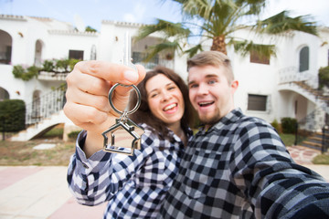 Obraz premium New Home, real estate and moving concept - Funny young couple showings keys from new house.