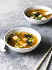 Japanese miso soup with oyster mushrooms in a white bowls with a spoon and white chopsticks on a grey background. copy space