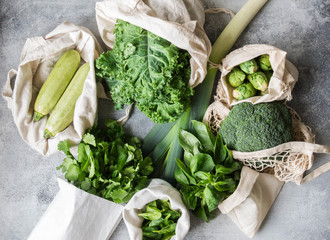 Healthy green vegan ingredients for cooking. Various clean green vegetables and herbs in textile bags. Products from the market without plastic. Zero waste concept flat lay.