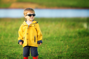 Cute little boy smiles in garden in sunglasses outdoors