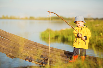 Picturesque scene of cute little boy fishing from wooden dock on magical lake at sunny summer day, vivid colors