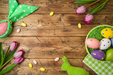 Easter holiday background with easter eggs in basket and tulip flowers on wooden table.