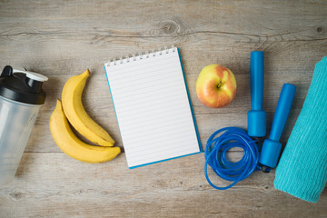 Fitness background with notepad, bottle for protein shake, healthy food and towel.