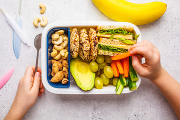 School healthy lunch box with sandwich, cookies, fruits and avocado on white background.