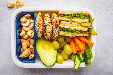 Healthy lunch box with sandwich, cookies, fruits and avocado on white background.