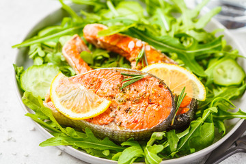 Fried red fish with arugula and cucumber salad in white plate.