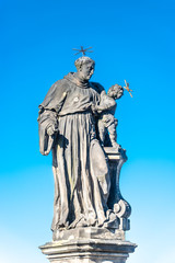 Fototapeta na wymiar Statue of fat and big priest with a child at the Charles Bridge in Prague at blue sky, Czech Republic, summer time