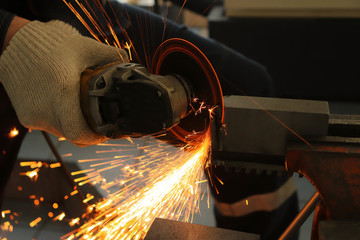 a gloved worker with a grinder cuts a carbide plate and this causes a lot of sparks