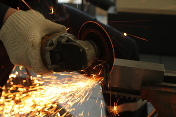 a gloved worker with a grinder cuts a carbide plate and this causes a lot of sparks