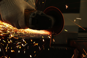 a gloved worker with a grinder cuts a carbide plate and this causes a lot of sparks