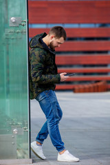 Young man texting on mobile phone on the city street.