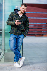 Young man texting on mobile phone on the city street.