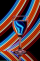 Wine glass isolated against a black background with colorful streaks of neon light painting behind them