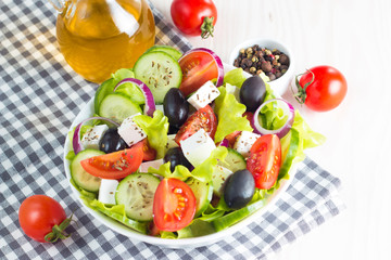 Fresh Greek salad made of cherry tomato, ruccola, arugula, feta, olives, cucumbers, onion and spices. Caesar salad in a white bowl on wooden background. Healthy organic diet food concept.