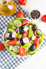 Fresh Greek salad made of cherry tomato, ruccola, arugula, feta, olives, cucumbers, onion and spices. Caesar salad in a white bowl on wooden background. Healthy organic diet food concept.